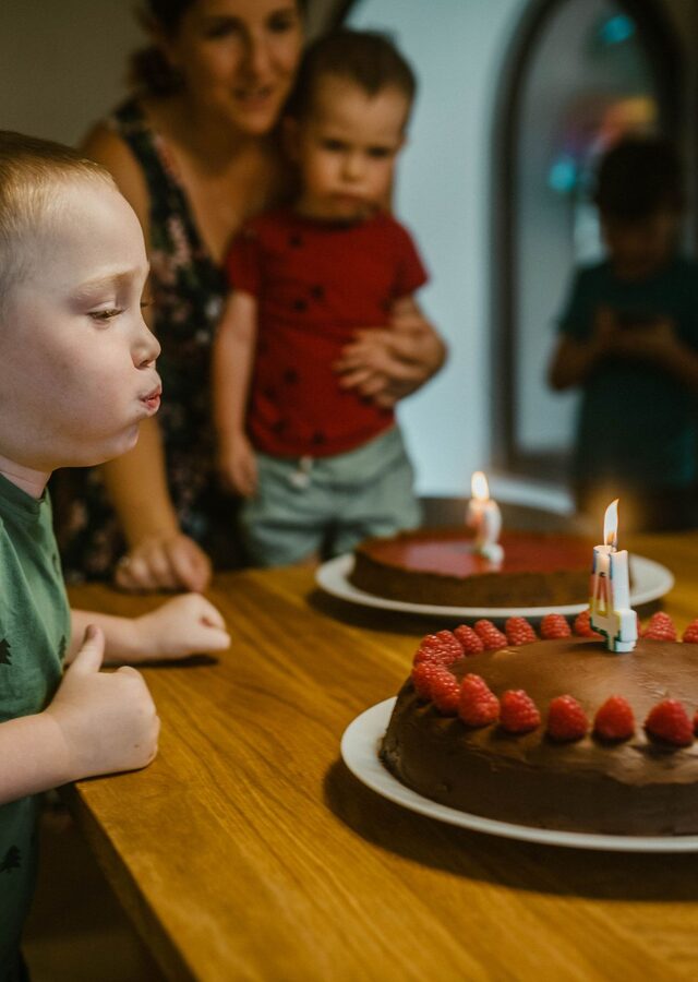 Recto de la carte : un petit garçon souffle les bougies d'un gâteau aux fraises, dans la cuisine