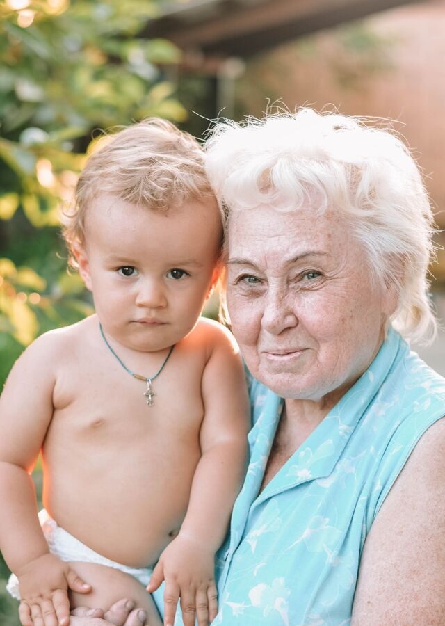 Recto de la carte : une grand-mère aux cheveux blancs pose sa joue contre celle de son petit-fils, dans la lumière du jardin